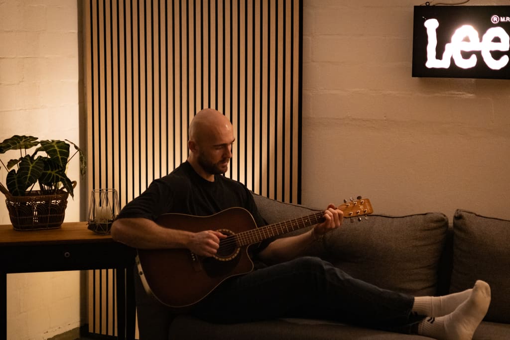 Tom spielt Akustikgitarre auf dem Sofa.